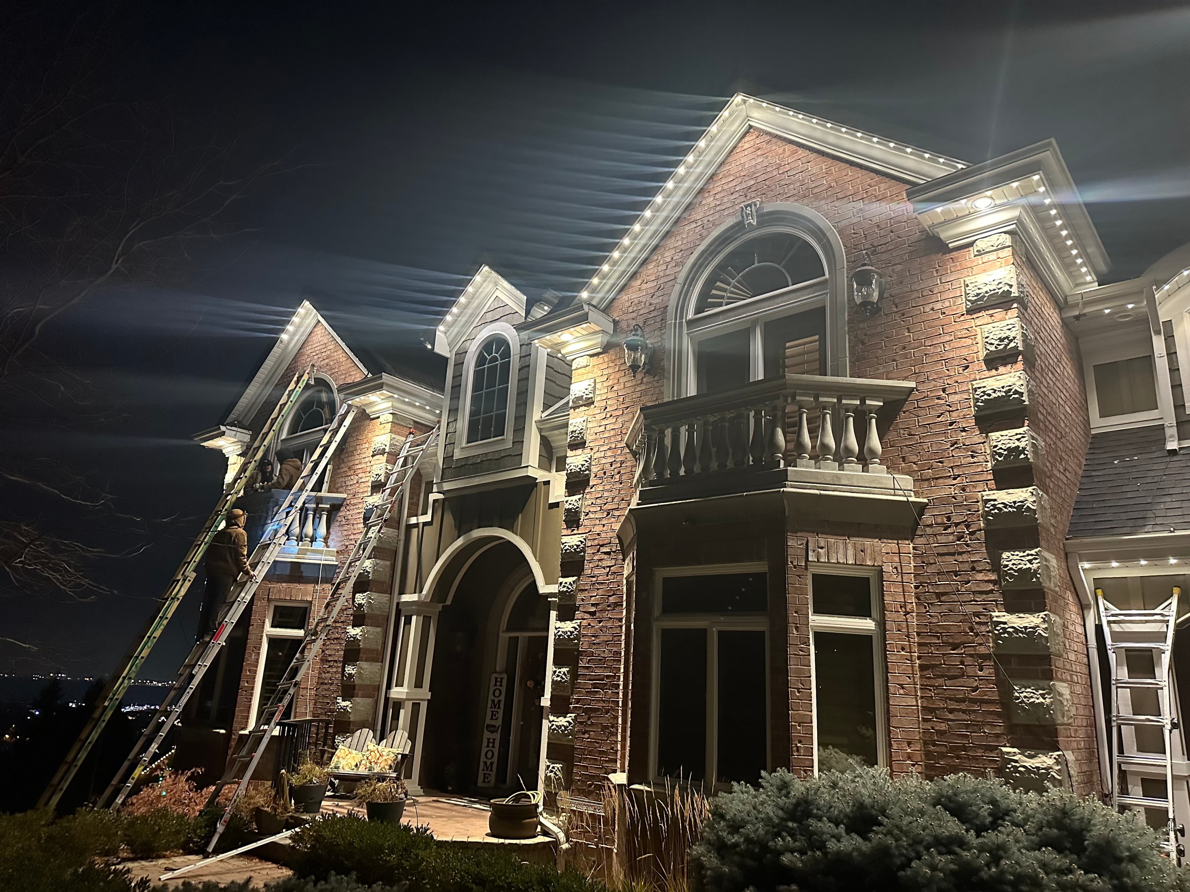 A crew installing lighting track along a roofline at night